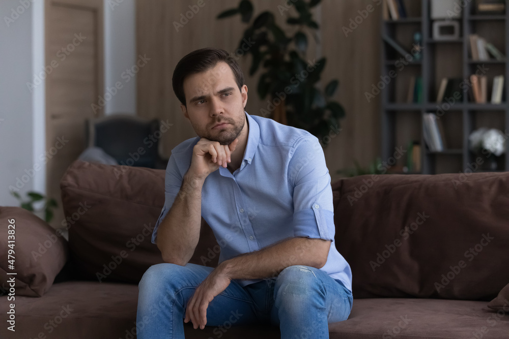 Thoughtful upset man looking in distance, sitting on couch at home alone, lost in thoughts about personal or relationships problem, thinking making difficult important decision, solving trouble Thoughtful upset man looking in distance, sitting on couch at home alone, lost in thoughts about personal or relationships problem, thinking making difficult important decision, solving trouble