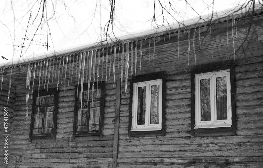 Long icicles hang from the roof of a wooden house to the very windows. Long icicles hang from the roof of a wooden house to the very windows.