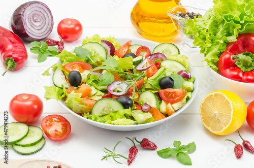 Healthy fresh vegetable salad with tomatoes, cucumbers and bell peppers in a plate on a white wooden background