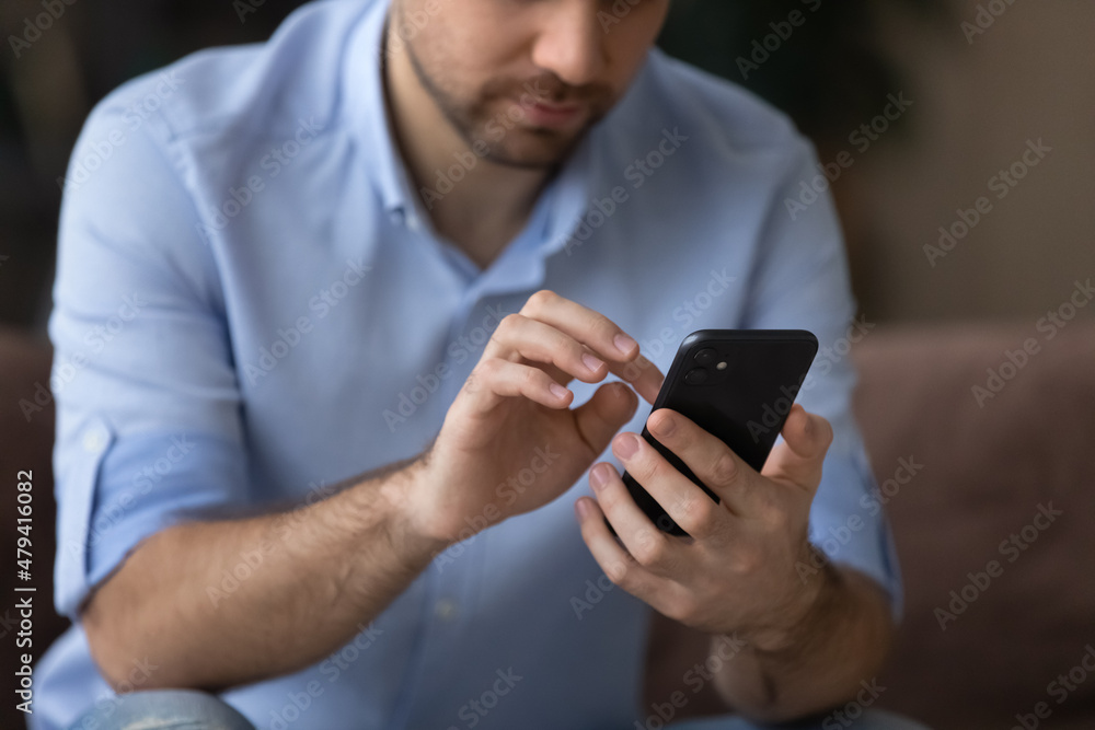 Fototapeta premium Cropped close up man using smartphone, typing on screen, focus on modern phone in male hands, chatting with friends in social network, browsing mobile device apps, playing game, shopping online