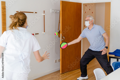 occupational therapist, kinesiologist rehabilitating an elderly man with tendinitis in his shoulder, catching a ball photo