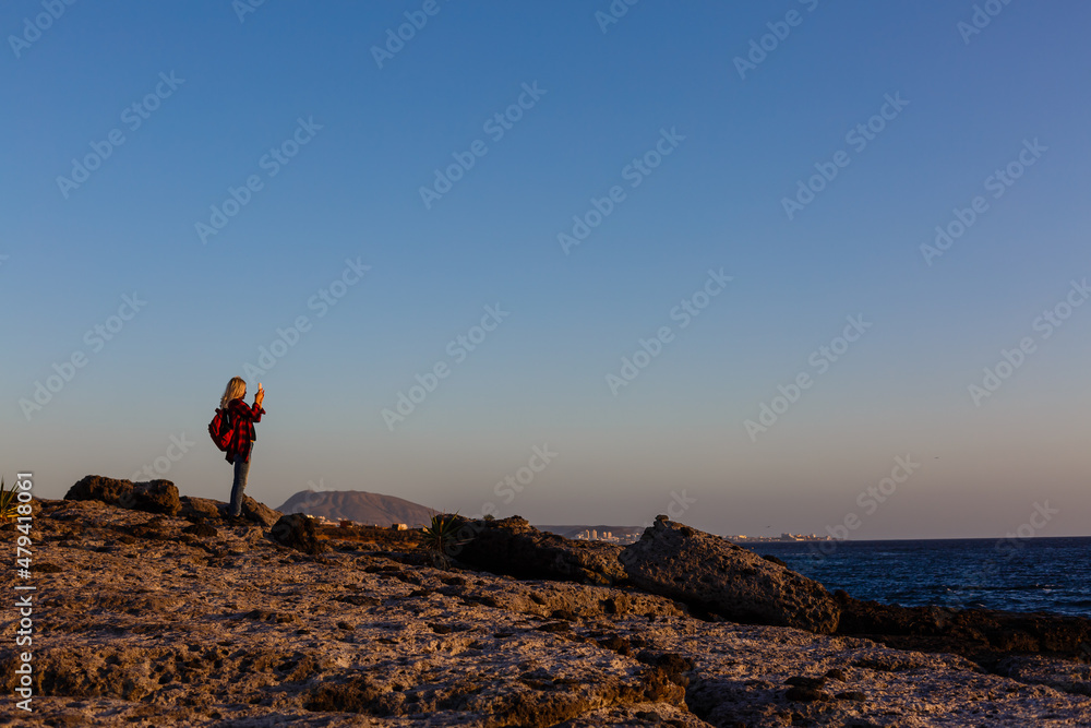 Women on volcanic rocks and blue ocean with waves, white foam and volcanic rocks. Canary Islands. The magnificent coast of the Atlantic Ocean