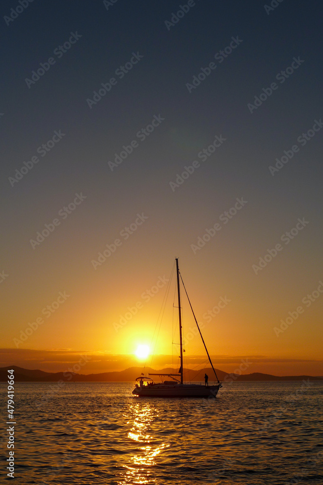 Silhouette of a sailboat on the Adriatic Sea with the sunset, mountains and clear, blue sky in the background. Zadar - Croatia