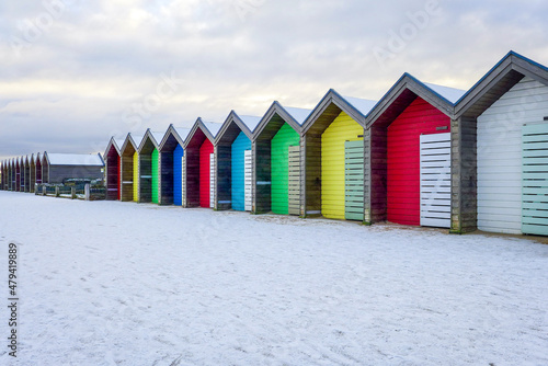 A row of vibrant, brightly coloured beach huts taken in winter with snow on the ground. Blyth, Northumberland - UK