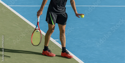 Young tennis player playing tennis on blue hard court. Male athlete with ball and racket is ready to serve at start of game. Sports background, copy space photo
