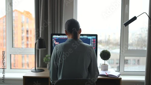 Back view of multiracial woman freelancer sitting at the table and typing on the keyboard, using trendy computer for remote work. Modern home office concept