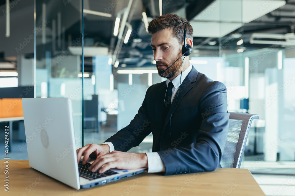 Business man in a modern office works at a computer, uses a headset for video calling, technical support Business man in a modern office works at a computer, uses a headset for video calling, technical support