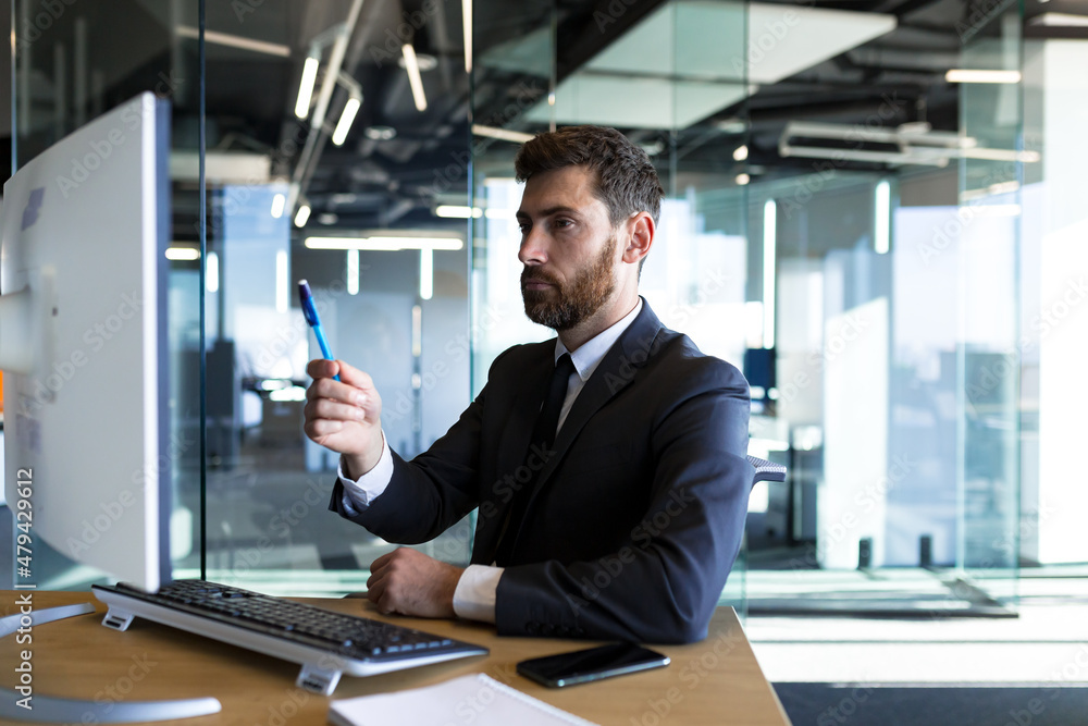 Serious and thoughtful male entrepreneur working in the office at the computer in a business suit Serious and thoughtful male entrepreneur working in the office at the computer in a business suit