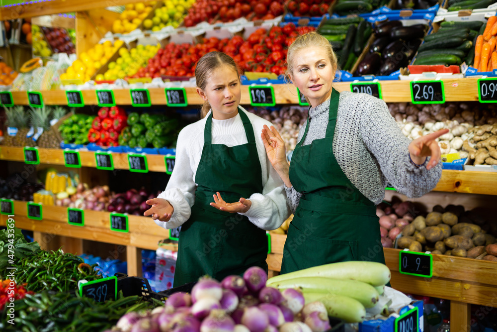 Grocery store clerk points hand to young trainee girl
