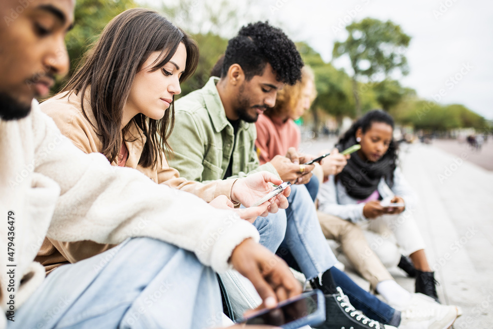 Group of young adult friends using smartphones outdoors - Addicted multiracial students chatting and sharing content on social media apps - Youth and technology concept Group of young adult friends using smartphones outdoors - Addicted multiracial students chatting and sharing content on social media apps - Youth and technology concept