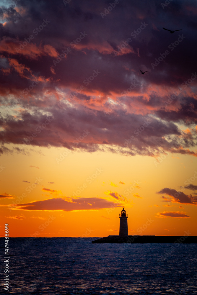 stunning sunset with cloudscape over the sea with a lighthouse in the foreground and clouds on the horizon 