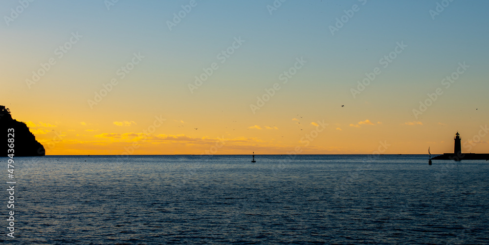 sunset over the sea with a clear sky and a lighthouse in the foreground 