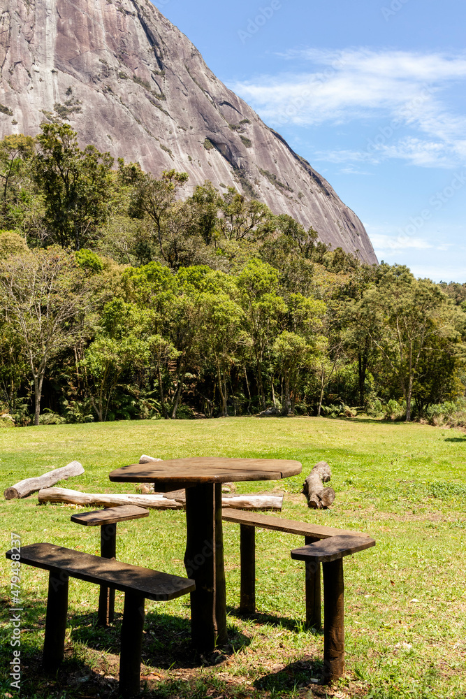 Wooden table and chairs in grassy picnic area with forest and rocky mountain in the background, Tres Picos State Park, Teresopolis, Rio de Janeiro, Brazil