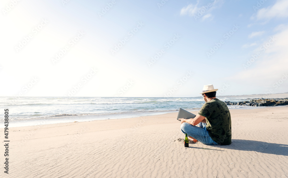 latin man sitting on the beach with a laptop alone drinking beer