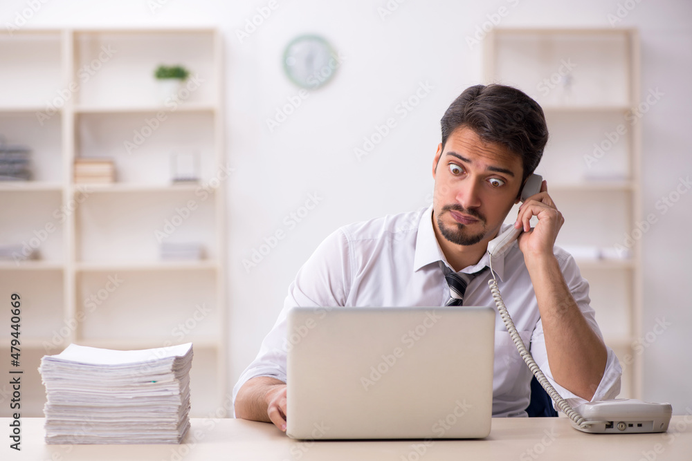 Young male employee unhappy with excessive work in the office Young male employee unhappy with excessive work in the office