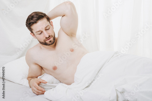 man wake up at morning in bed shirtless and stretch arm