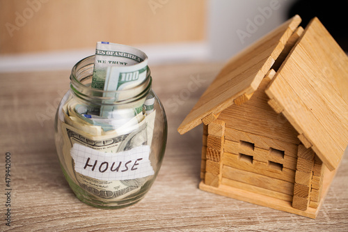 Dollar bills in glass jar and text house on wooden table.