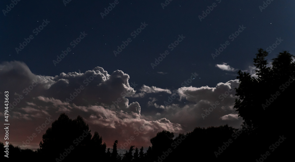 Nubes con cielo estrellado y cambio de colores, silueta de arboles 