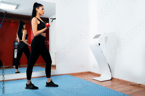 Side view, fit young woman in gym working out next to EMS machine 
