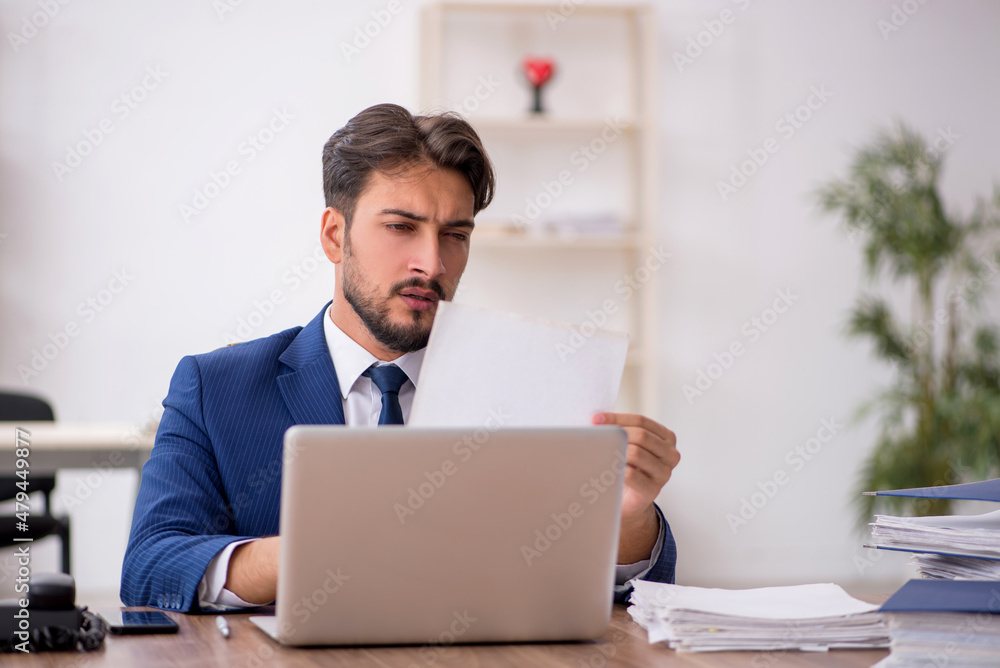 Young male employee unhappy with excessive work in the office Young male employee unhappy with excessive work in the office