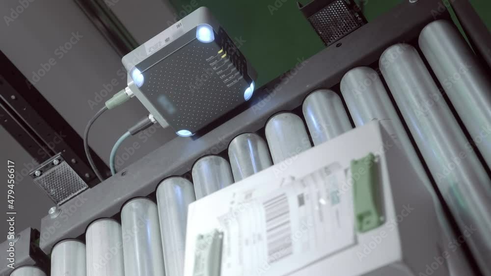 An industrial laser sensor on a roller conveyor detects the passage of a white cardboard box, detects it and enters into a database. Closeup. Closeup An industrial laser sensor on a roller conveyor detects the passage of a white cardboard box, detects it and enters into a database. Closeup. Closeup