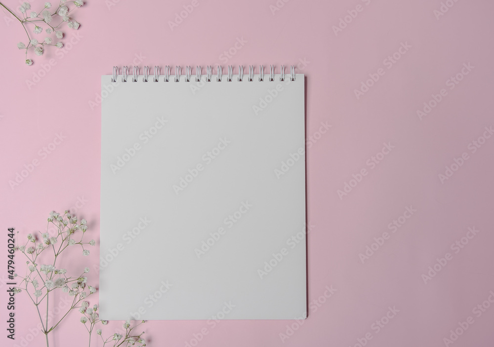 White spiral notebook with white smoll flowers. Copy space for the design. Blank square spiral notepad on pink background White spiral notebook with white smoll flowers. Copy space for the design. Blank square spiral notepad on pink background