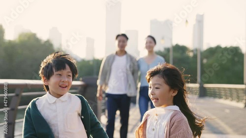 happy asian family with two children taking a walk in city park