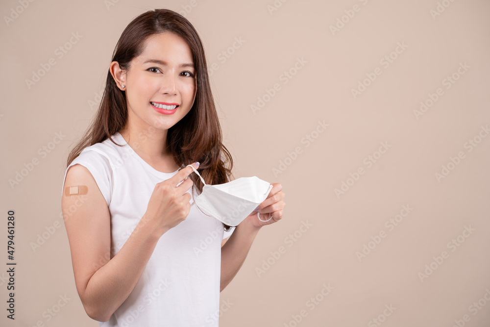 Young beautiful asian woman smiling and showing arm after vaccine injection Coronavirus. She holds a mask, flu vaccination and immunization. Studio background looking at camera. Young beautiful asian woman smiling and showing arm after vaccine injection Coronavirus. She holds a mask, flu vaccination and immunization. Studio background looking at camera.
