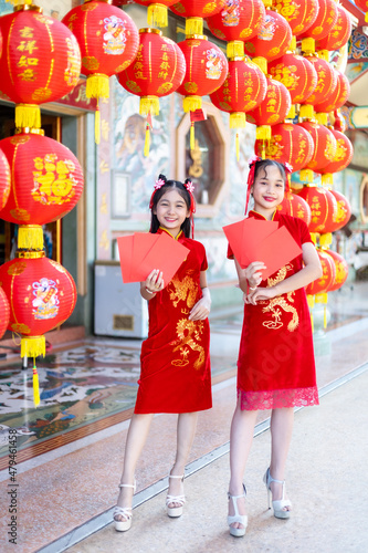 Asian Two girl wearing red traditional Chinese cheongsam decoration holding red envelopes in hand and lanterns with the Chinese text Blessings written on it Is a Fortune blessing for Chinese New Year