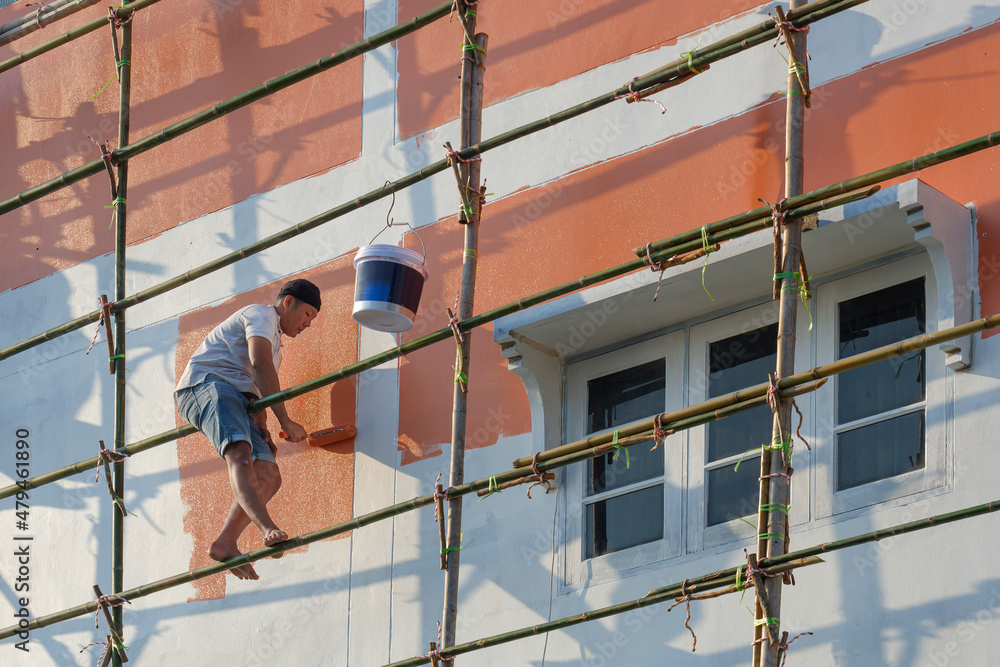 Low angle view of Asian painter on wooden scaffold is painting wall outside of the old house building, home renovation and improvement concept