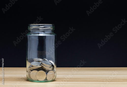 coin in glass jar on wood and black background. Business financial and saving money and investments concept.