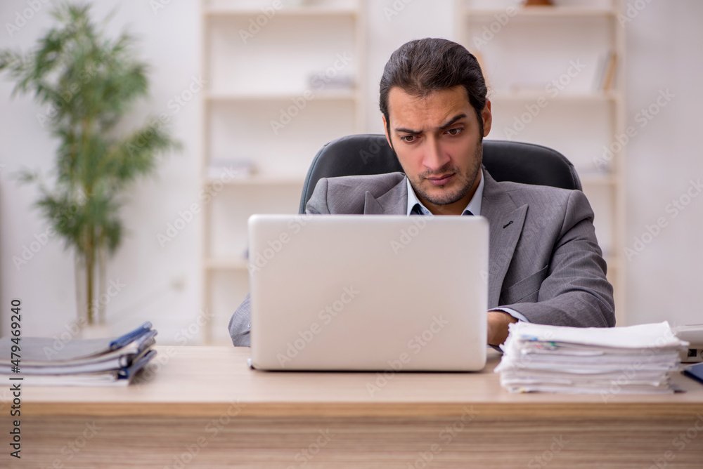 Young male employee unhappy with excessive work in the office Young male employee unhappy with excessive work in the office