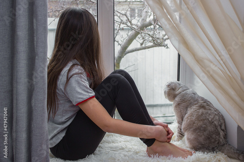 Fotografi The child is resting on the windowsill and looking out the window with a lop-eared cat