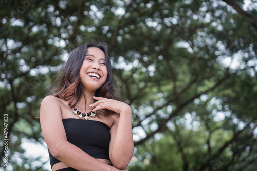 A happy young woman laughing but in a composed manner. Standing outside at a park. photo