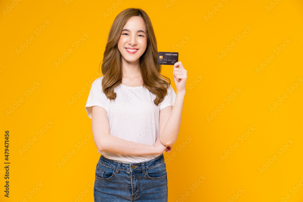 Cheerful beautiful Asian woman in white t-shirt and holding mockup credit card on yellow background. Cheerful beautiful Asian woman in white t-shirt and holding mockup credit card on yellow background.