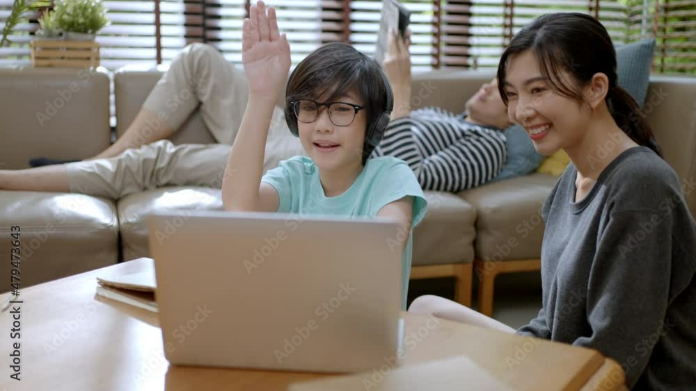 remote learn online and study at home concept.asian boy child student use laptop remotely learn with mother and answer question from online teacher in living room at home during coronavirus outbreak. remote learn online and study at home concept.asian boy child student use laptop remotely learn with mother and answer question from online teacher in living room at home during coronavirus outbreak.