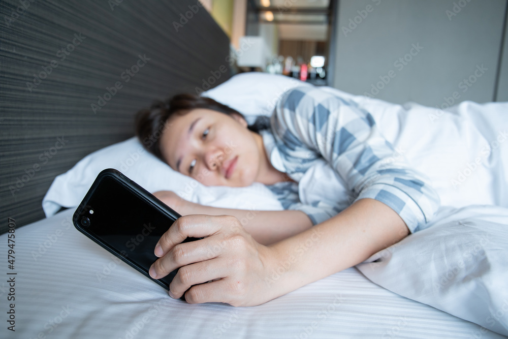 Lazy Asian young woman trying to snooze awaking alarm clock in smartphone. Lazy Asian young woman trying to snooze awaking alarm clock in smartphone.