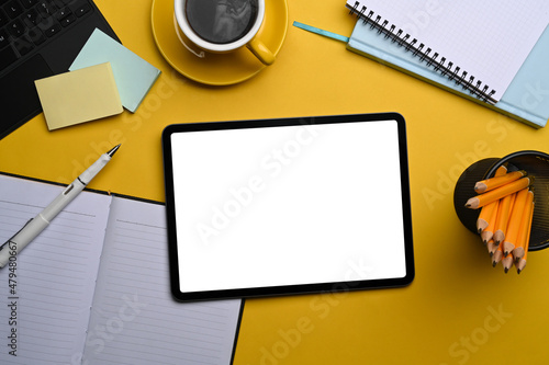 Top view mock up digital tablet with white screen and supplies on yellow background.