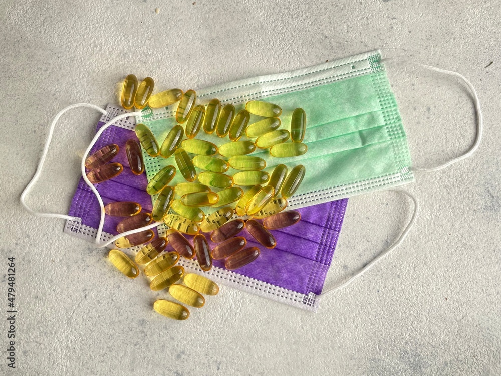 Cod liver capsules on coloured face masks. Health protection concept. Consume Omega 3 and wear