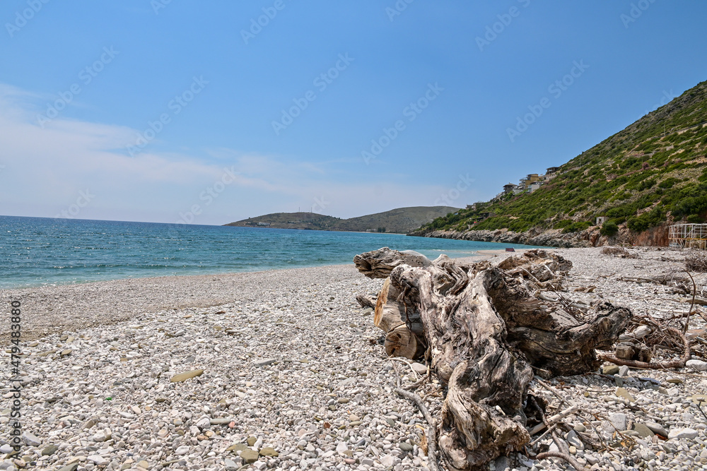 strand-am-meer-in-albanien-mit-treibgut-bergen-und-blauem-himmel-stock