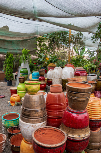 Several ceramic pots of different sizes and colors, next to ornamental plants and flowers inside a plant nursery. © JuanSt