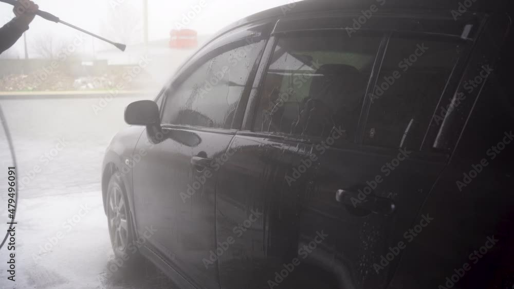a man washes a car using a pressure washer on the street. a man washes a car using a pressure washer on the street.