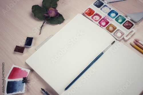 Decorative layout of art materials on the desktop paints, dried flowers, an empty notebook with a brush for inserting pictures