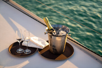 Champagne bottle in ice bucket with champagne glass for serving to passenger tourist on luxury catamaran boat sailing in the ocean at summer sunset. Tropical travel vacation sail yacht trip concept