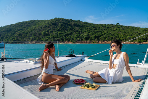 Valokuvatapetti Portrait of Caucasian female friends enjoy luxury lifestyle eating fresh fruit while catamaran boat sailing together