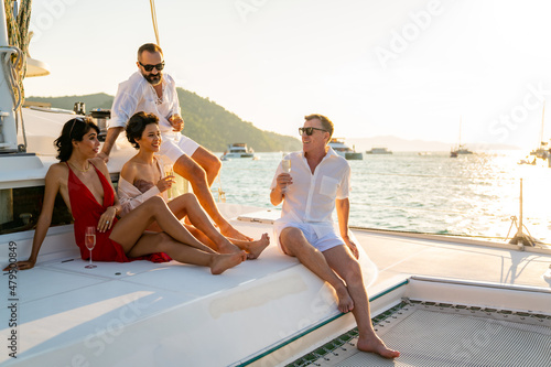 Photography Group of man and woman friends enjoy party drinking champagne with talking together while catamaran boat sailing at summer sunset