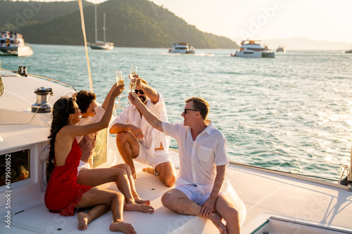 Obraz na plátne Group of man and woman friends enjoy party drinking champagne with talking together while catamaran boat sailing at summer sunset