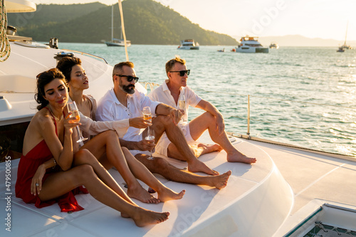 Group of man and woman friends enjoy party drinking champagne with talking together while catamaran boat sailing at summer sunset. Male and female relax outdoor lifestyle on tropical travel vacation © CandyRetriever 