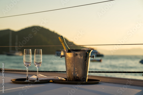 Fototapeta Champagne bottle in ice bucket with champagne glass for serving to passenger tourist on luxury catamaran boat sailing in the ocean at summer sunset