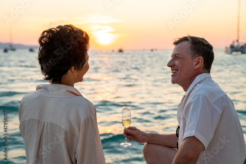 Canvas Print Caucasian couple enjoy outdoor luxury party drinking champagne with talking together while catamaran boat sailing at sunset